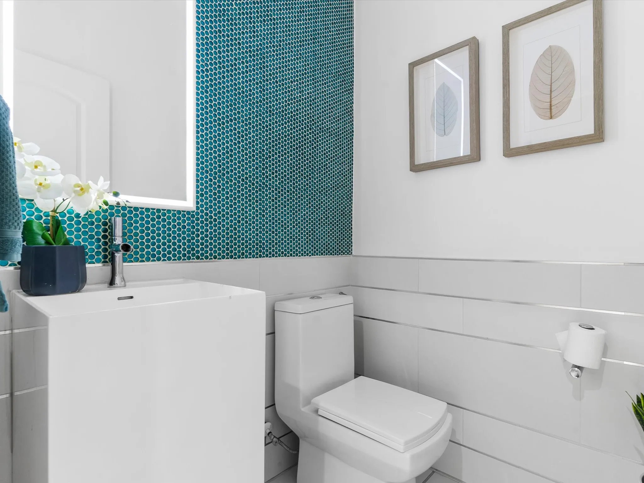Bathroom featuring a pedestal sink, white tile wainscoting with silver trim, and a teal penny tile accent wall
