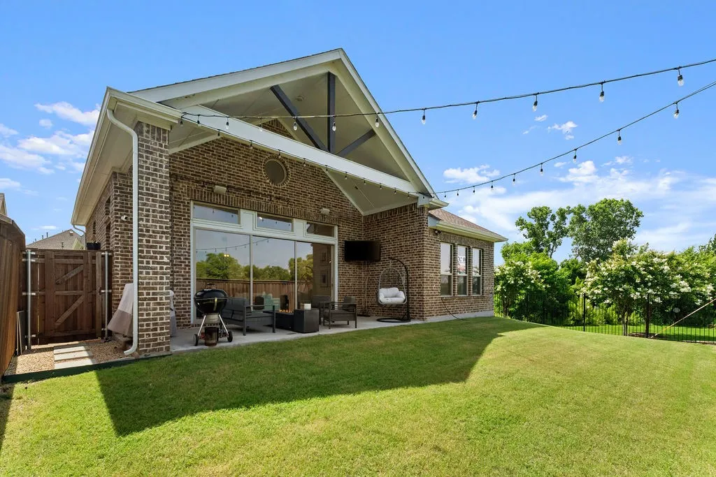 Expansive backyard featuring a covered patio with vaulted ceiling, string lighting, full-light sliding glass door, and brick exterior