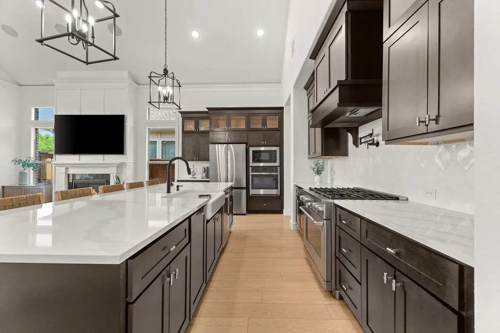 Gourmet kitchen featuring a large central island with an integrated sink, dark wood cabinetry, stainless steel appliances, a gas range, and wood-finish flooring