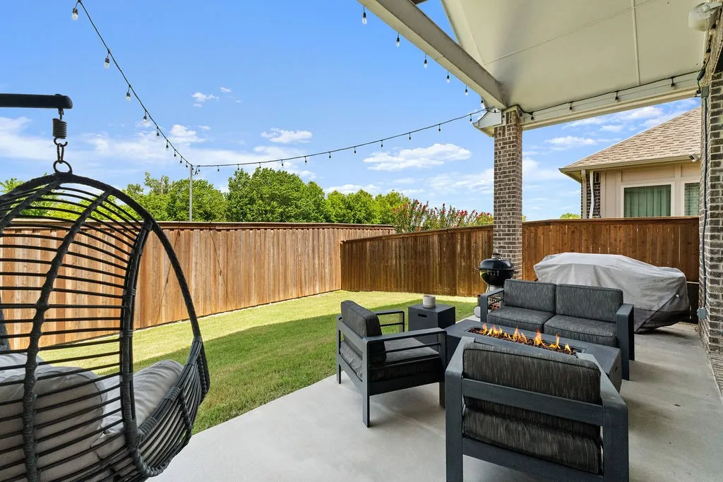 Covered patio with string lighting, concrete flooring, brick columns, a wood fence, and a grass lawn