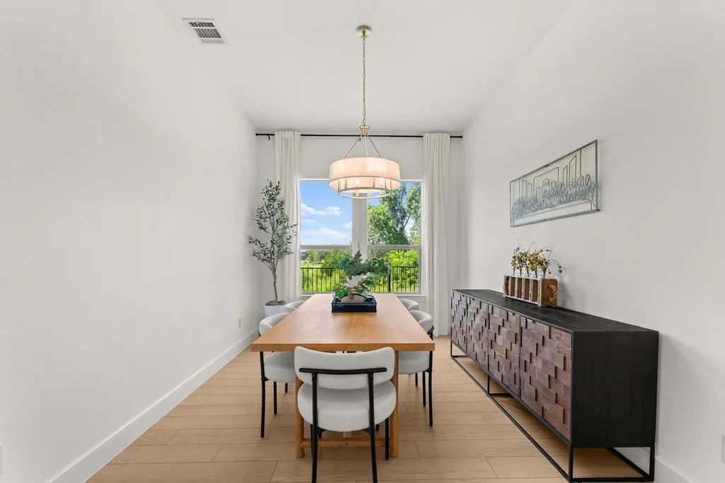 Spacious dining area featuring wood-finish flooring, a contemporary chandelier, a large window with outdoor visibility, white walls, and white baseboards