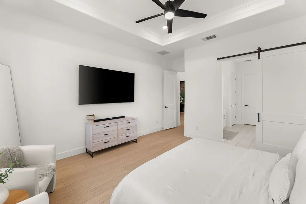 Recessed tray ceiling with a black ceiling fan, wood-finish flooring, white walls, and a barn door entry