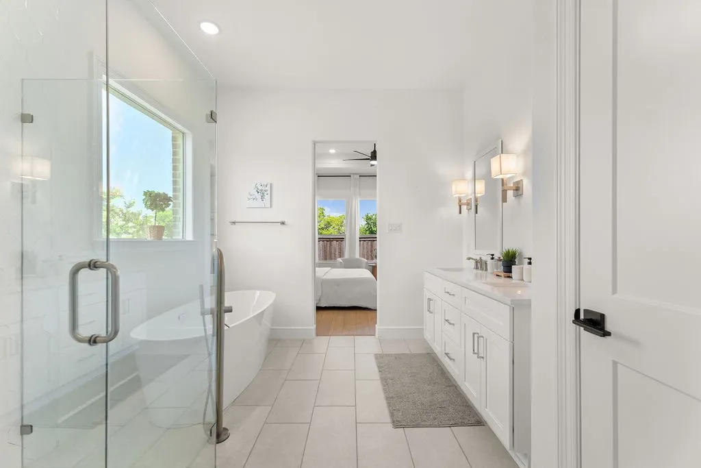 Modern bathroom featuring a freestanding soaking tub, glass-enclosed shower, white tile flooring, and a double vanity with stone countertop