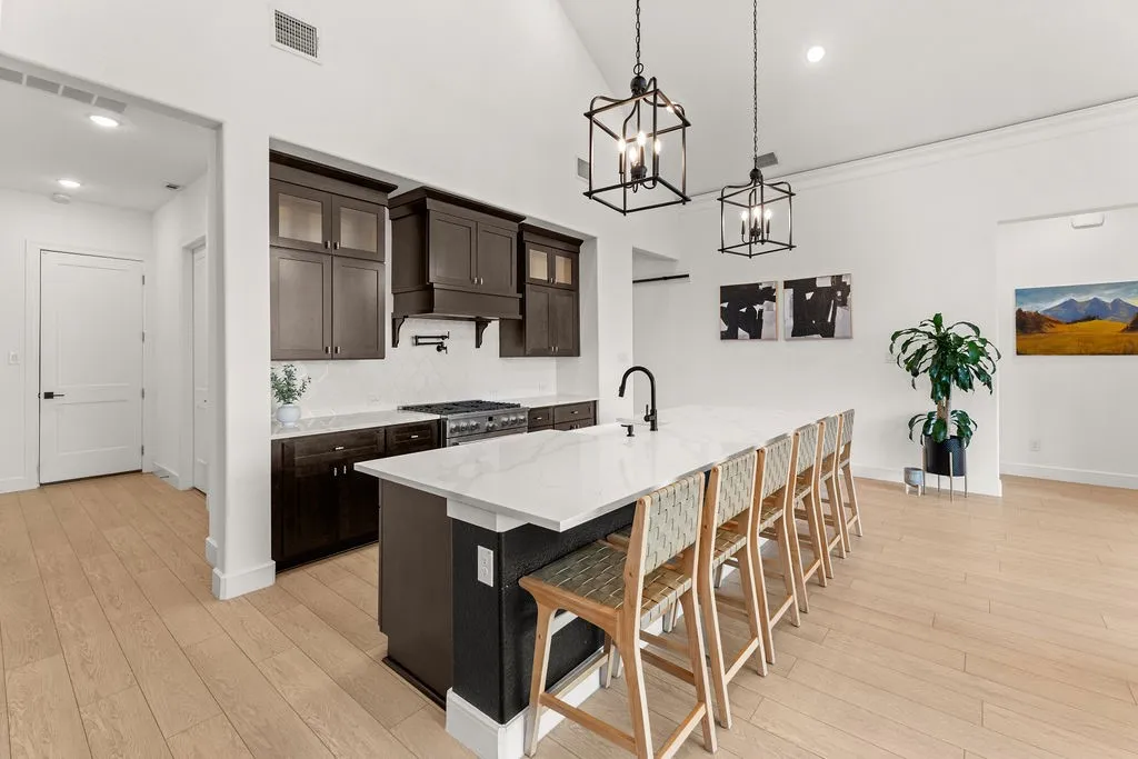 Kitchen featuring a large central island with seating, dark wood-finish cabinetry, a gas range with a pot filler, a tiled backsplash, and recessed lighting