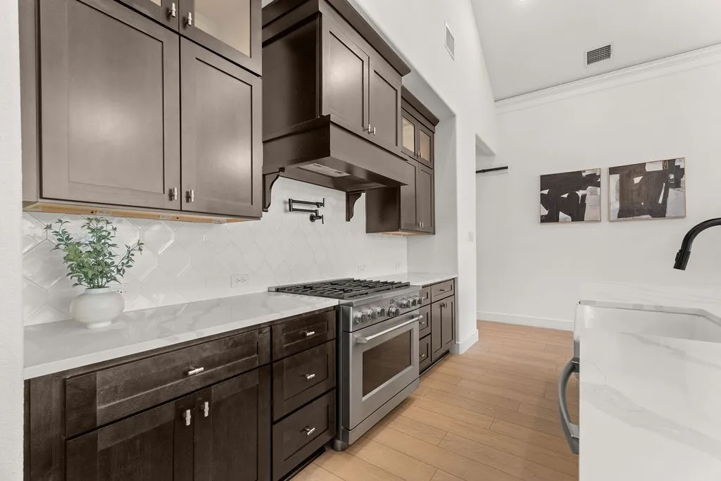 Gourmet kitchen featuring dark wood cabinetry, white countertop surfaces, a stainless steel range oven, and a white geometric tile backsplash