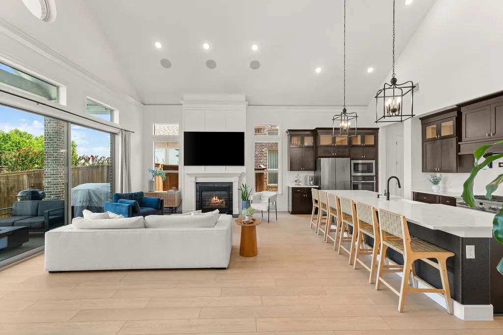 Open-concept living space featuring vaulted ceilings, wood-finish flooring, a contemporary fireplace, and a gourmet kitchen with a spacious island