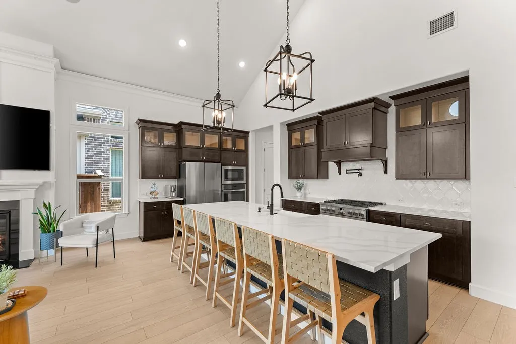 Vaulted ceilings complement the kitchen featuring an expansive center island with seating, dark wood cabinetry, stainless steel appliances, a range with pot filler, and light wood-finish flooring