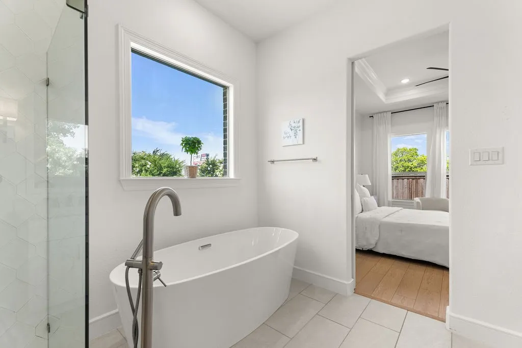 Freestanding soaking tub with a floor-mounted brushed nickel faucet, large window, and separate glass-enclosed shower featuring geometric tile