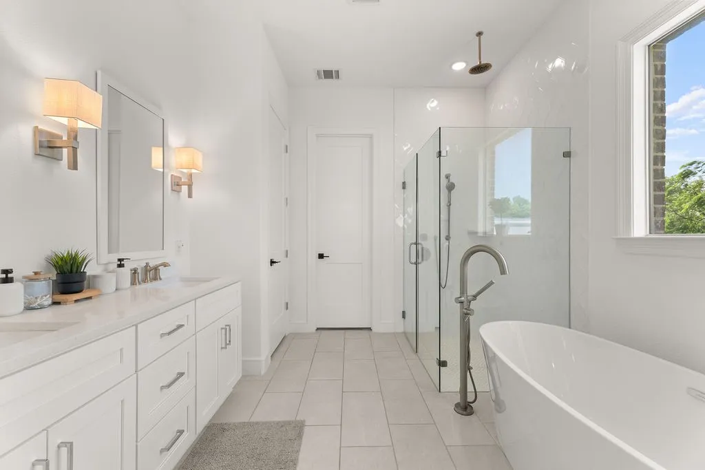 Spacious bathroom featuring a freestanding soaking tub, a glass-enclosed shower, a dual vanity with white cabinetry, and light-toned tile flooring