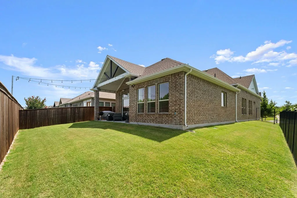 Expansive backyard featuring a manicured lawn, brick exterior, covered patio, and a privacy fence