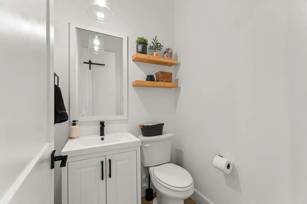 Powder room featuring a white single-sink vanity with matte black hardware, a rectangular framed mirror, and two floating wood shelves