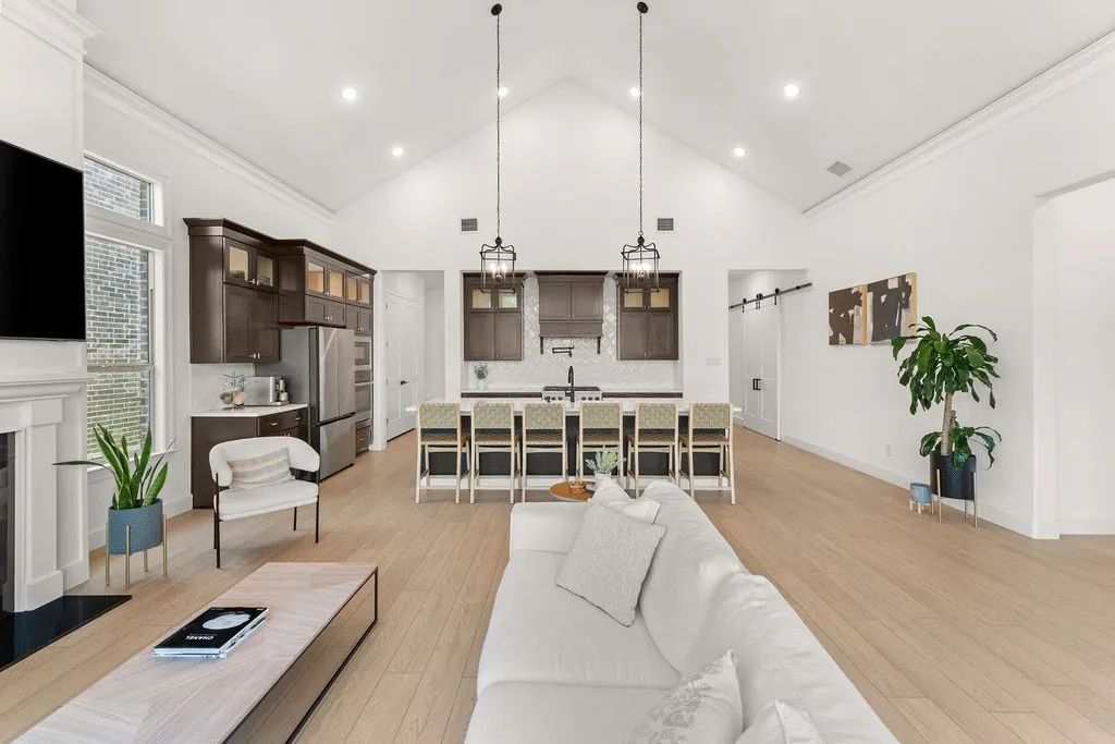 Expansive open-concept living space featuring vaulted ceilings, light wood-finish flooring, and a stone fireplace
