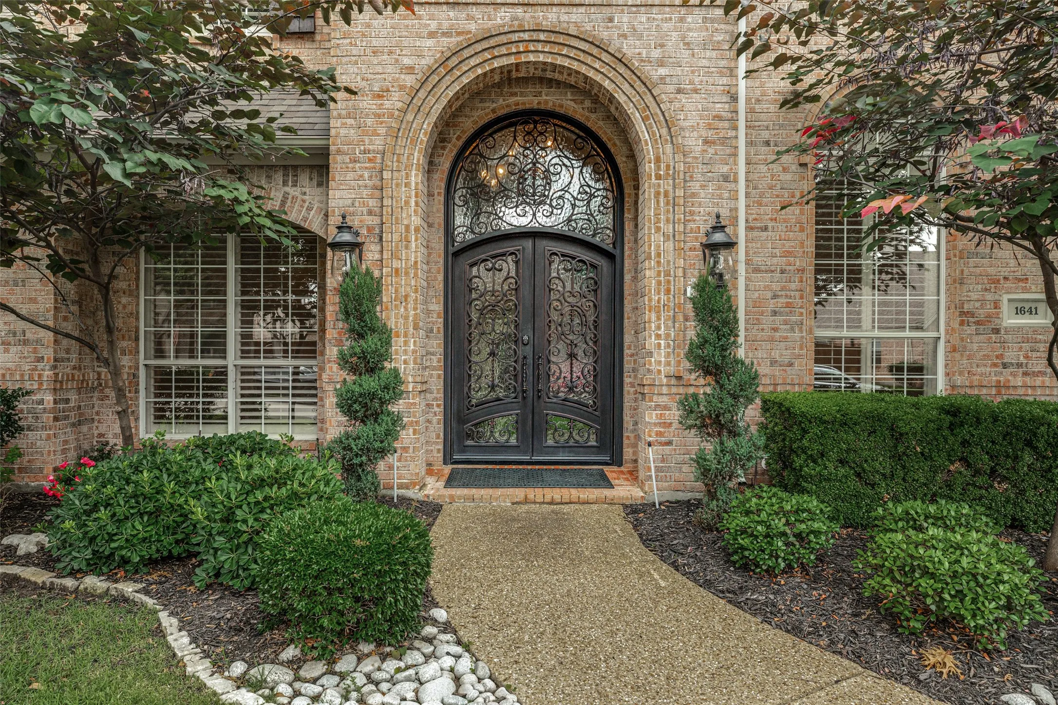 The timeless durable brick exterior is enhanced with a stunning updated front door.  Heavy iron double doors are embellished with decorative scroll designs both on the doors and the large arched transom window above. Distinctive brickwork sets off the arched entry to the front porch and creates a horizontal water table design.  A pair of coach lanterns add illumination for visitors.  Holiday lights specifically designed for the home will stay with the property.