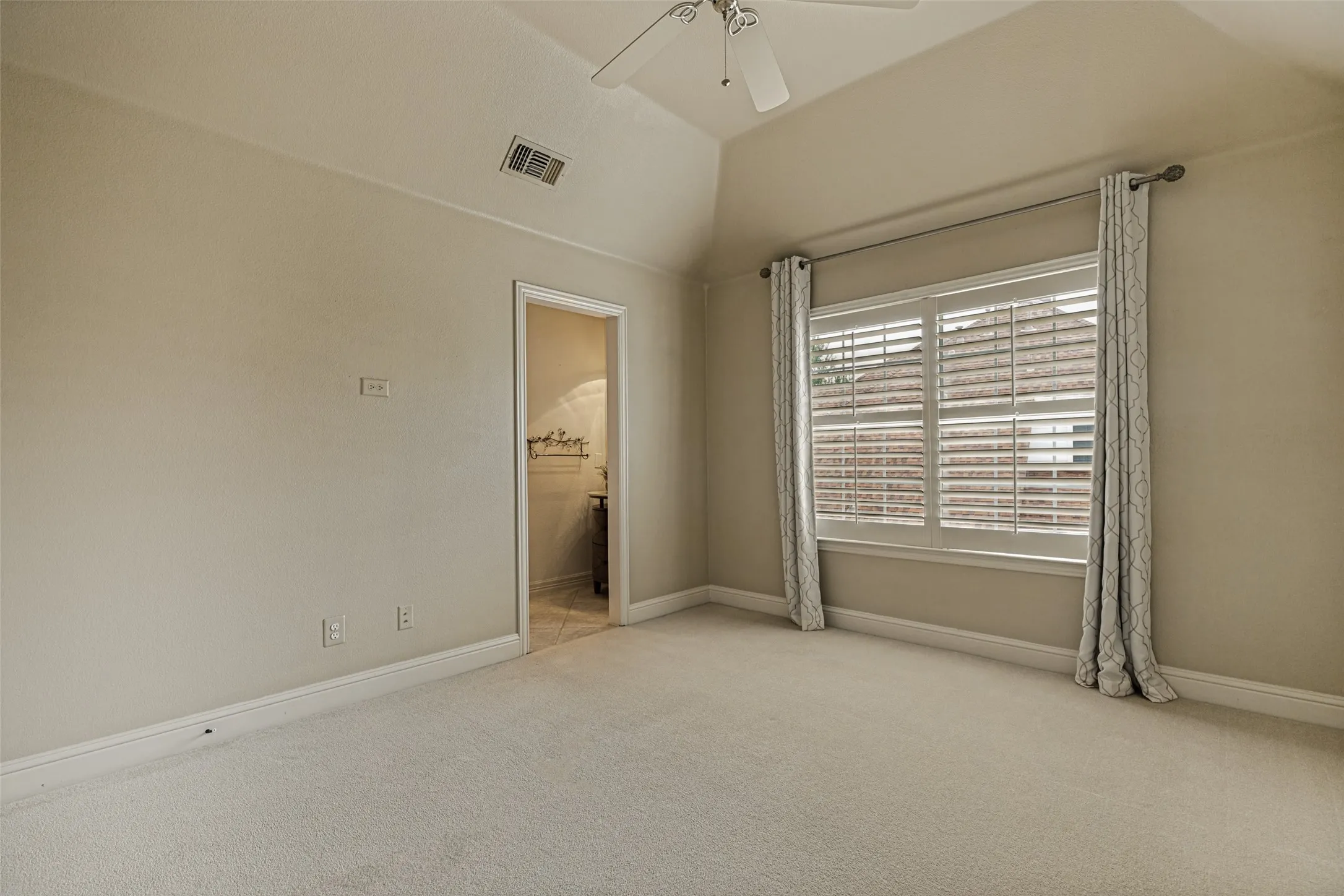 The remaining upstairs bedroom has a pair of wide windows overlooking the side of the home.  Shutters and drapes decorate the windows.  This room also has a raised ceiling with a fan and soft neutral carpet below, and it also has access to the Jack and Jill bath.