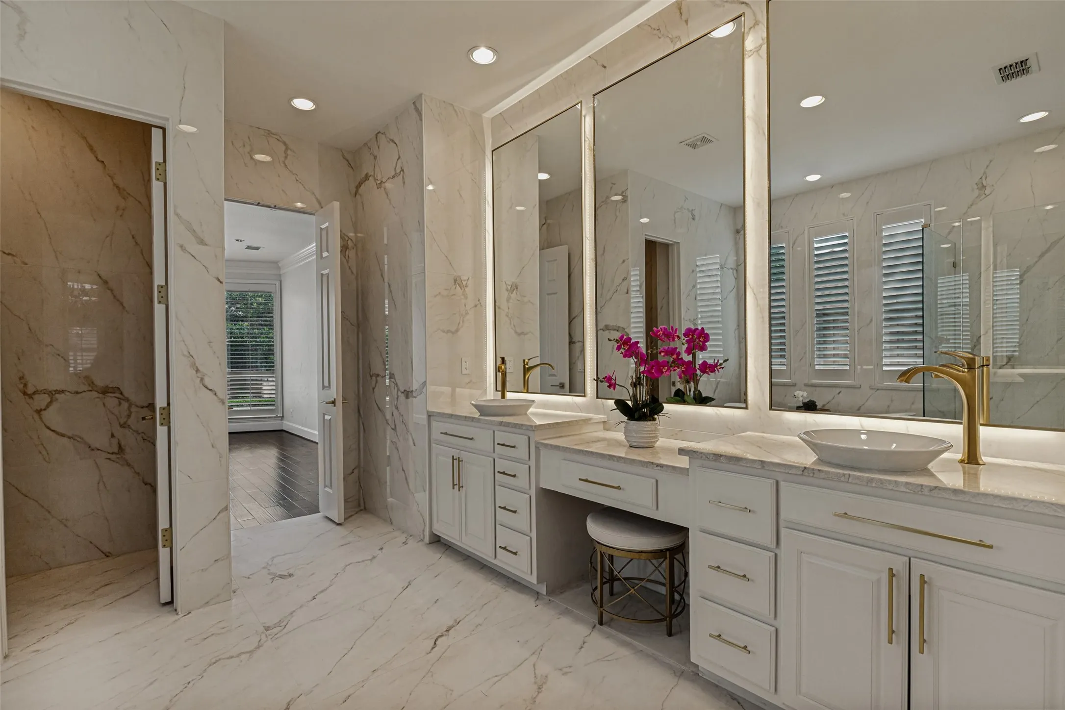 White vessel sinks top the quartz countertops.  Tall backlit mirrors create a sense of additional volume. Premium champagne gold hardware is on the cabinets and drawers as well as plumbing fixtures and door hardware. The porcelain tile continues into the toilet enclosure.
