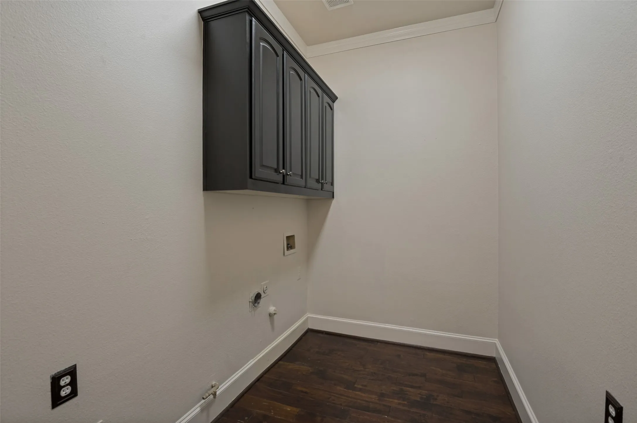 The oversized laundry room is large enough to allow a second refrigerator.  A bank of cabinets over the location for the washer and dryer provide storage.  Wood is on the floor and crown molding dresses up even this utility room.  Electric plugs are available on both sides of the room, making an ironing board or rechargeable vacuum easy to use.  Located near the kitchen, this room completes the downstairs of the home.