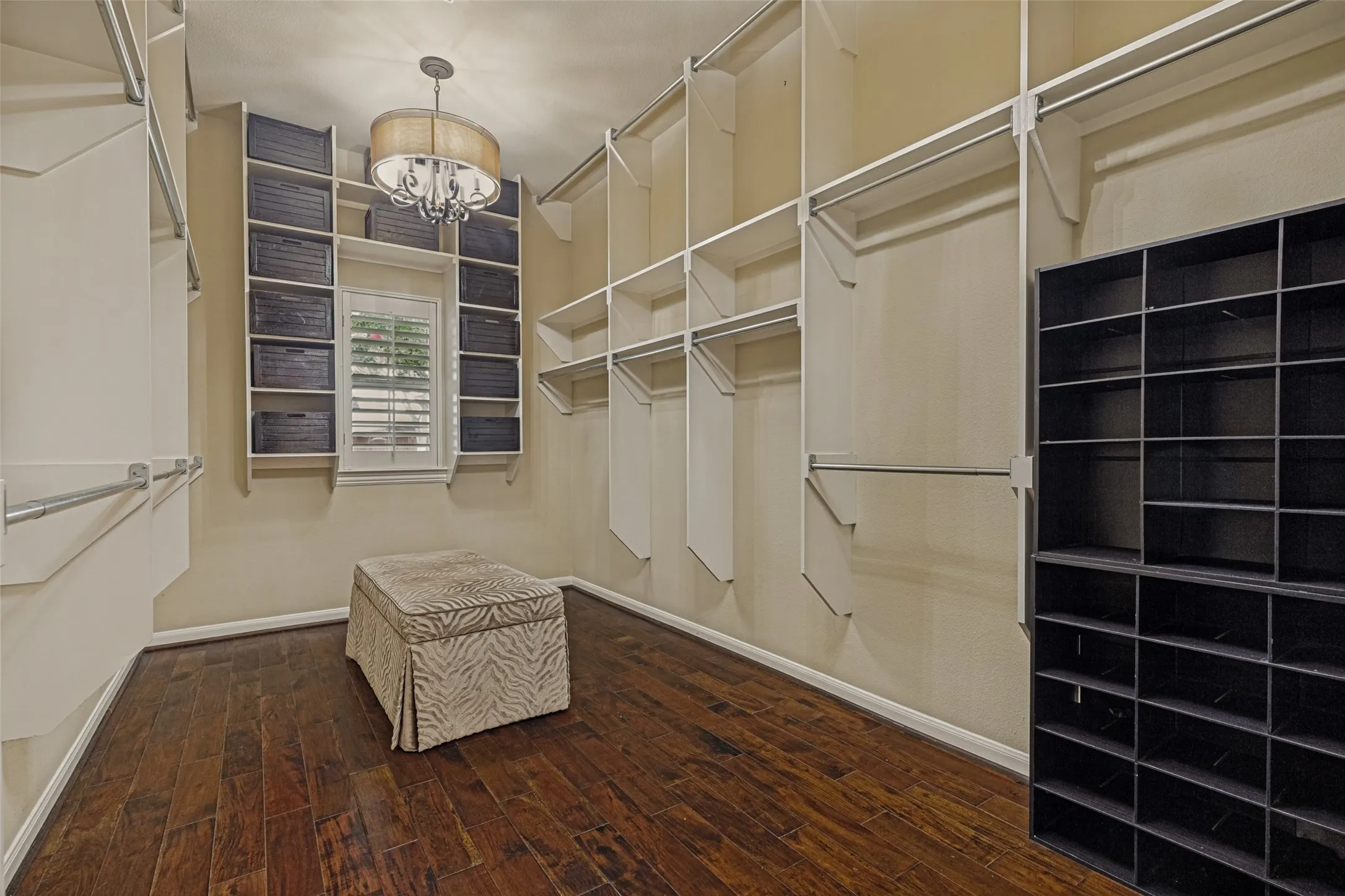 Everyone appreciates a substantial closet, and this one is just that!  Wood floors keep it tidy and built in and freestanding cubbies store shoes purses and folded clothes.  A window with a shutter allows natural light and a pair of pretty chandeliers bring the glamour from the bath to the closet.  And, the cute bench  and baskets stay.