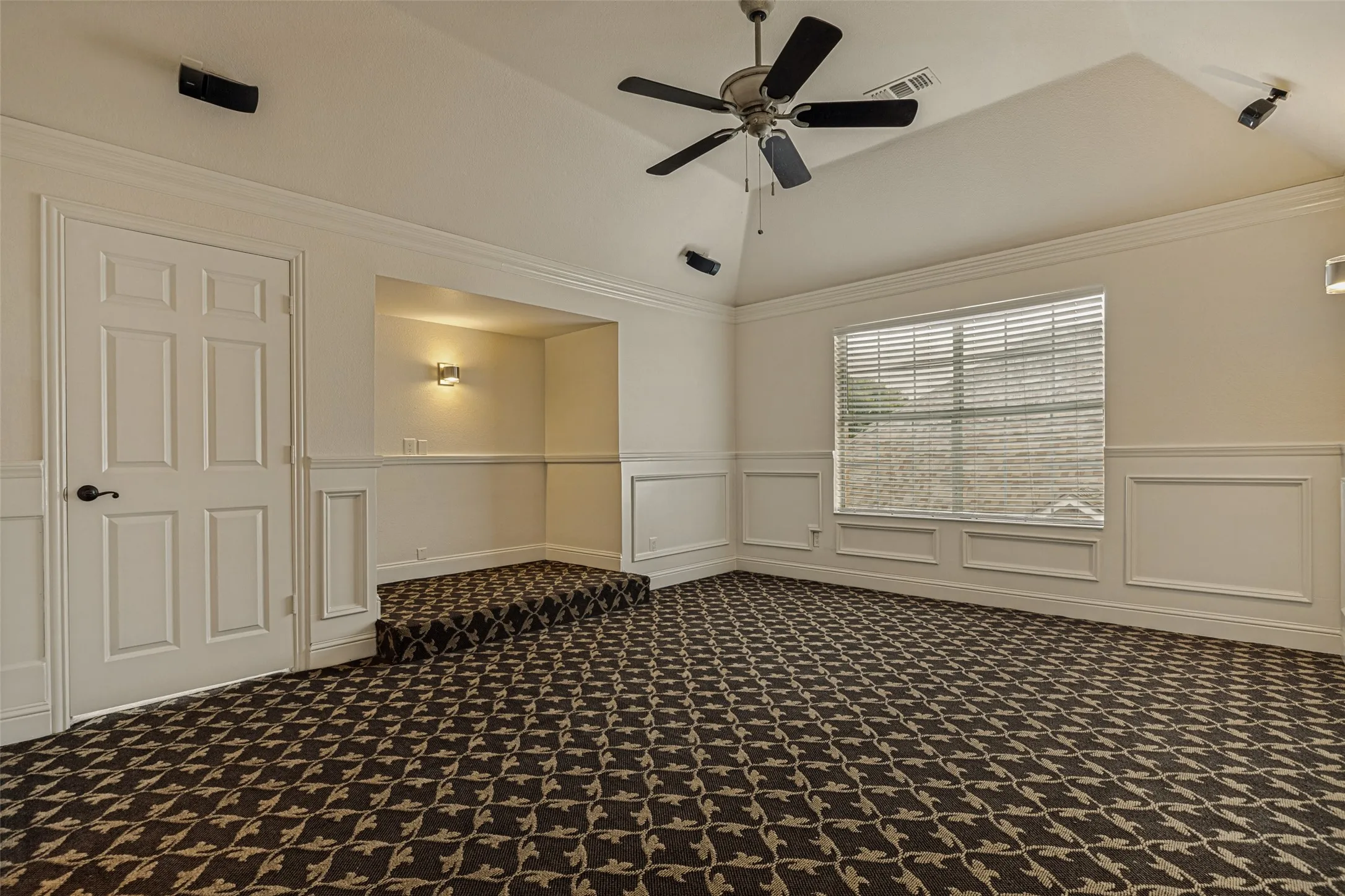 What a great spot for family movie night or watching your favorite sports playoff game!  This sizable bedroom was re-imagined to become a terrific media room.  Theater style carpet is on the floor.  A niche with a wall sconce was created to allow two lounge chairs to have raised seating.  Wood wainscotting was added to enhance the walls and crown molding is at the base of the tray ceiling.  Windows with blinds are available to use if desired.