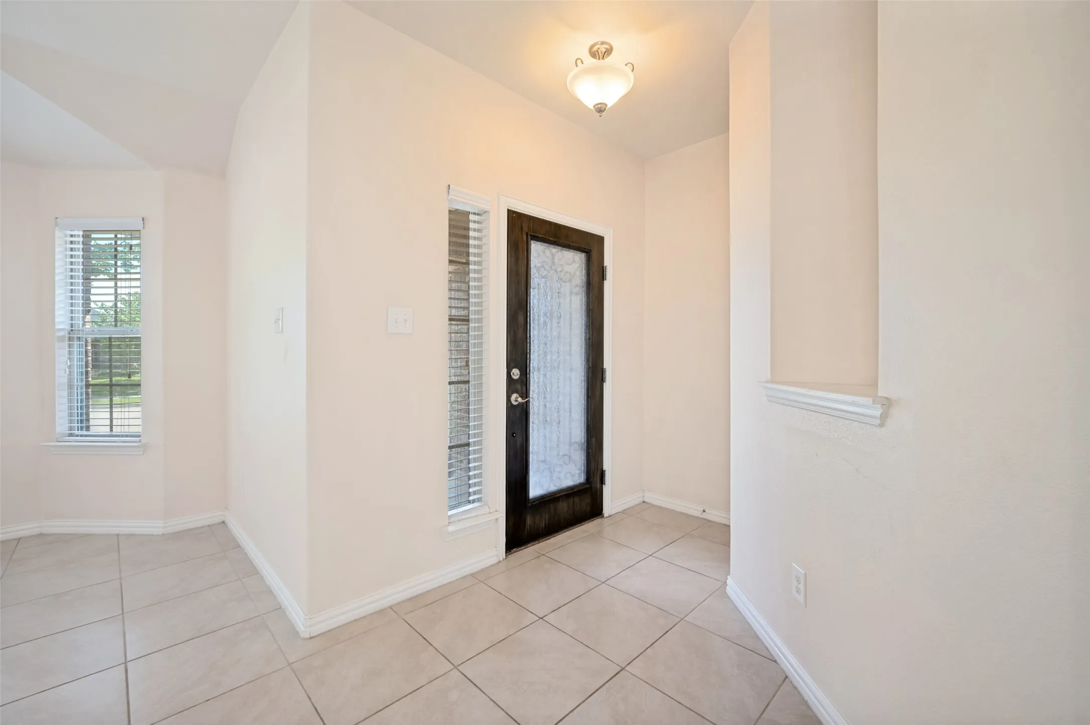 Entryway featuring light-toned tile flooring, a dark wood-finish door with frosted glass, and a transom window