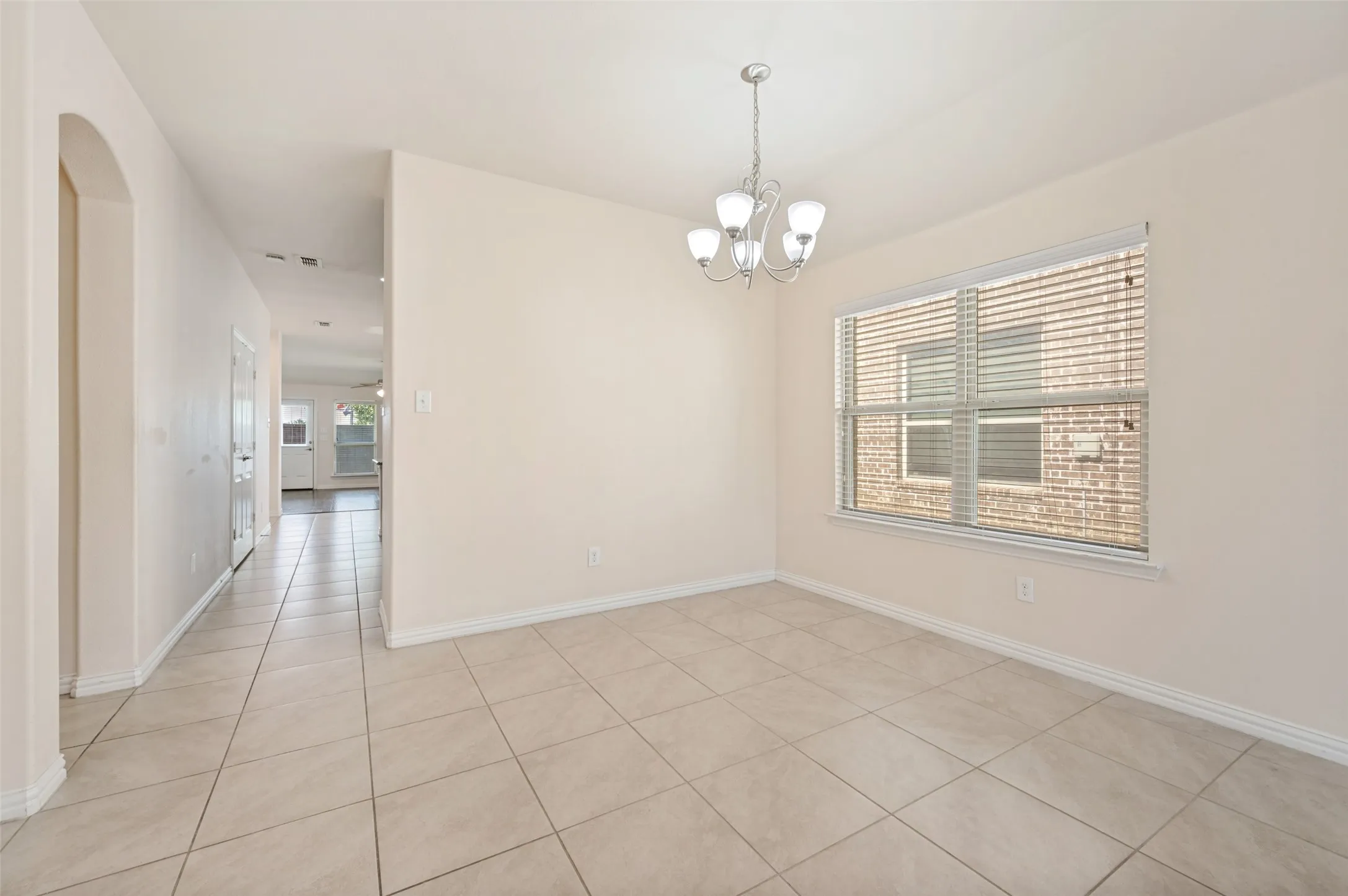 Tiled flooring throughout this open space, featuring a window with horizontal blinds and a four-light chandelier