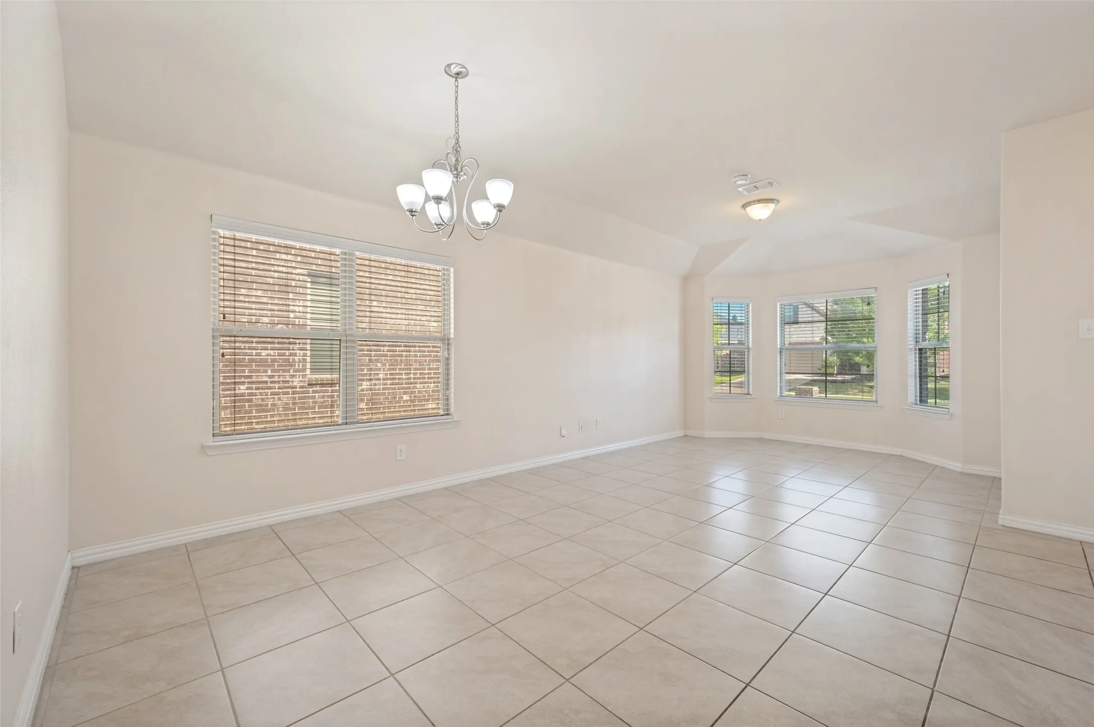 Spacious room featuring neutral-toned walls, tile flooring, and a chandelier lighting fixture