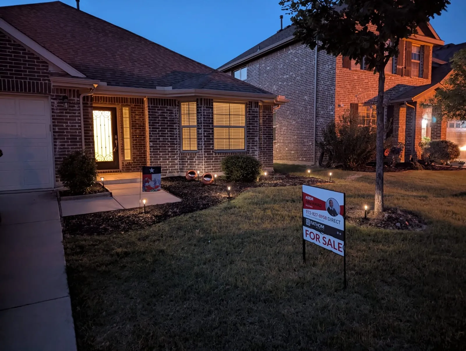 This charming brick home offers exceptional evening curb appeal with welcoming exterior accent lighting, beautifully manicured landscaping, and a classic glass front door.