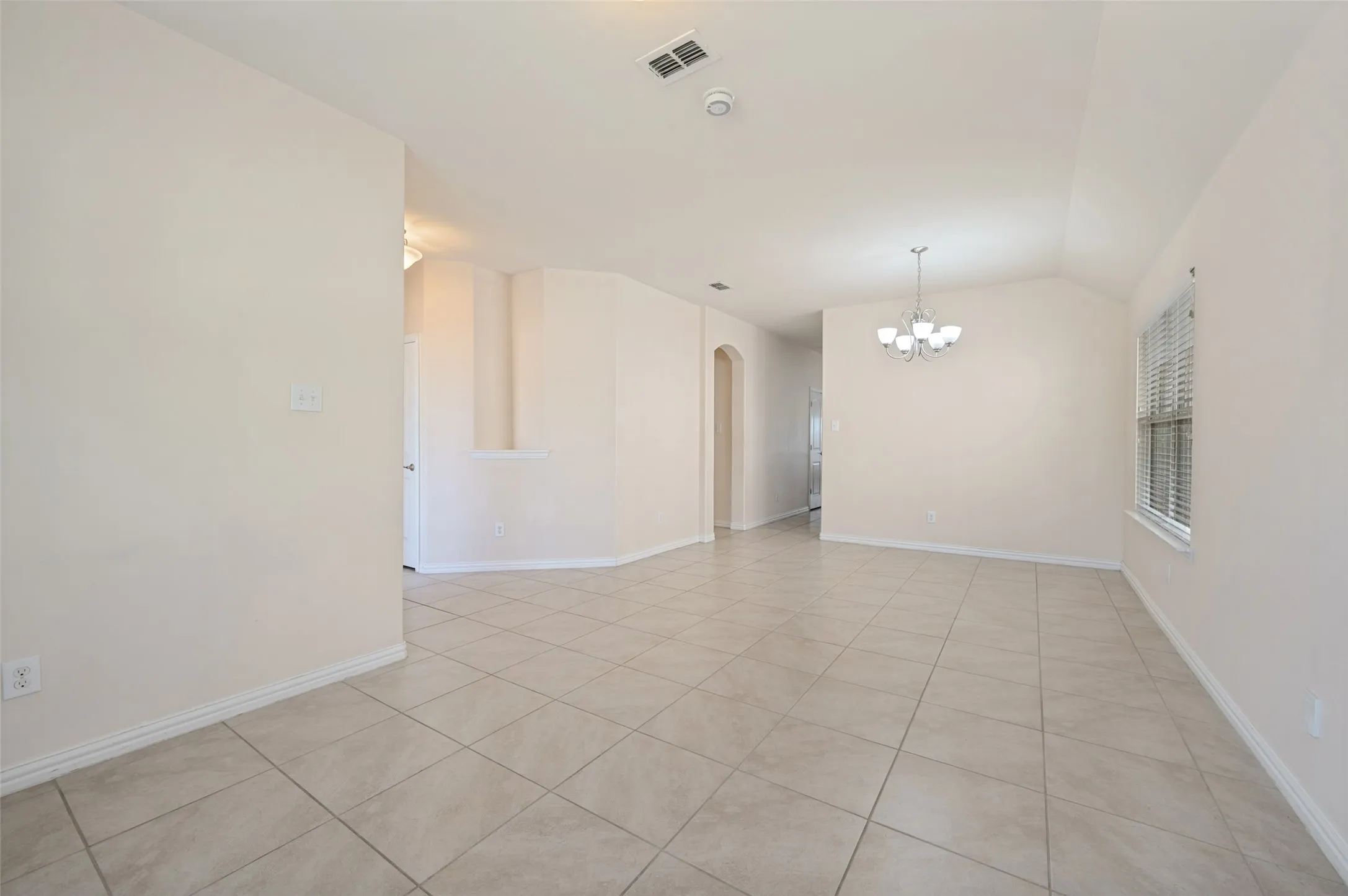 Spacious room featuring tile flooring, vaulted ceiling, and a large window with blinds