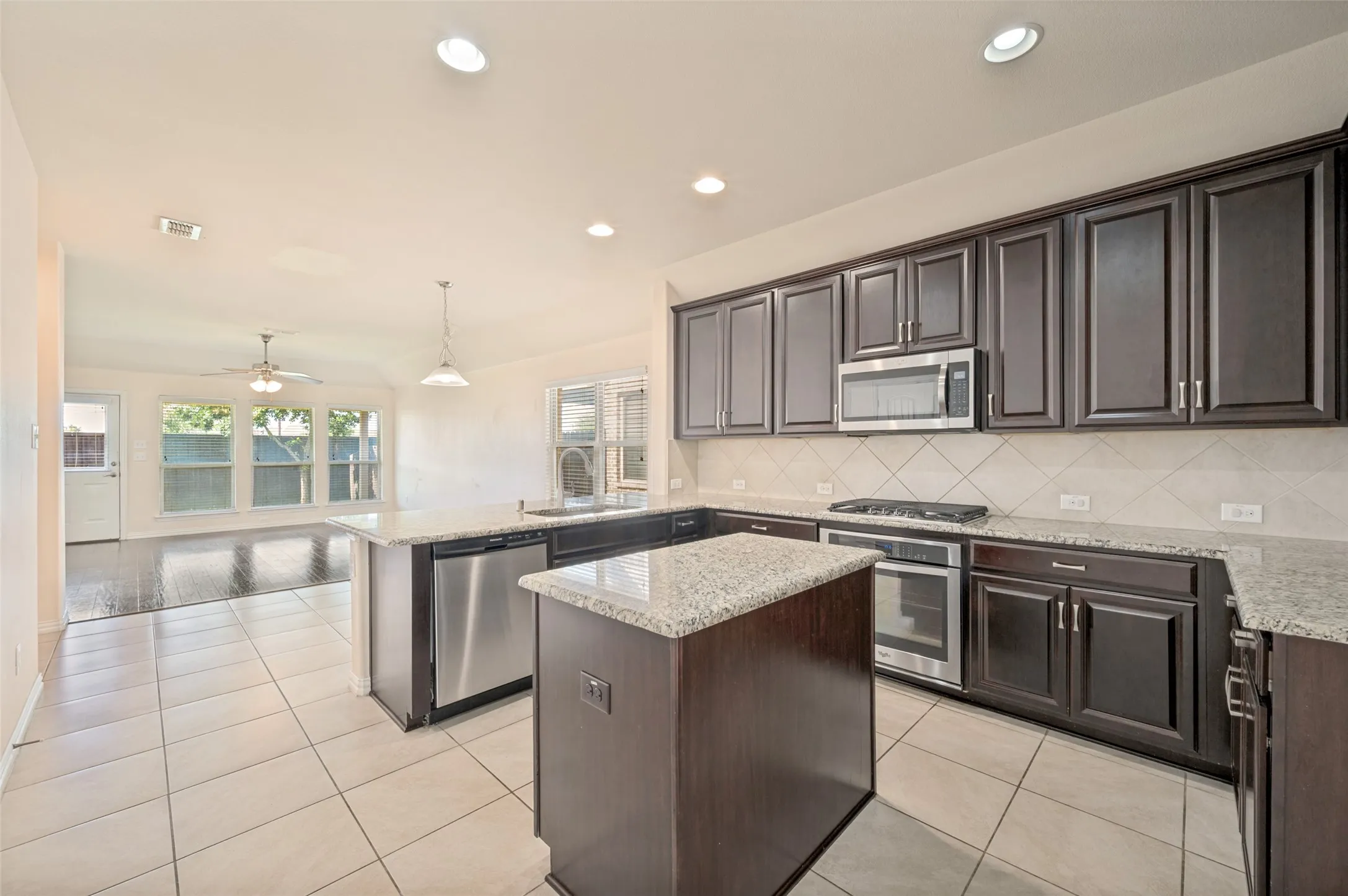Kitchen featuring a center island with granite countertops, dark wood-finish cabinetry, stainless steel appliances, and tile flooring