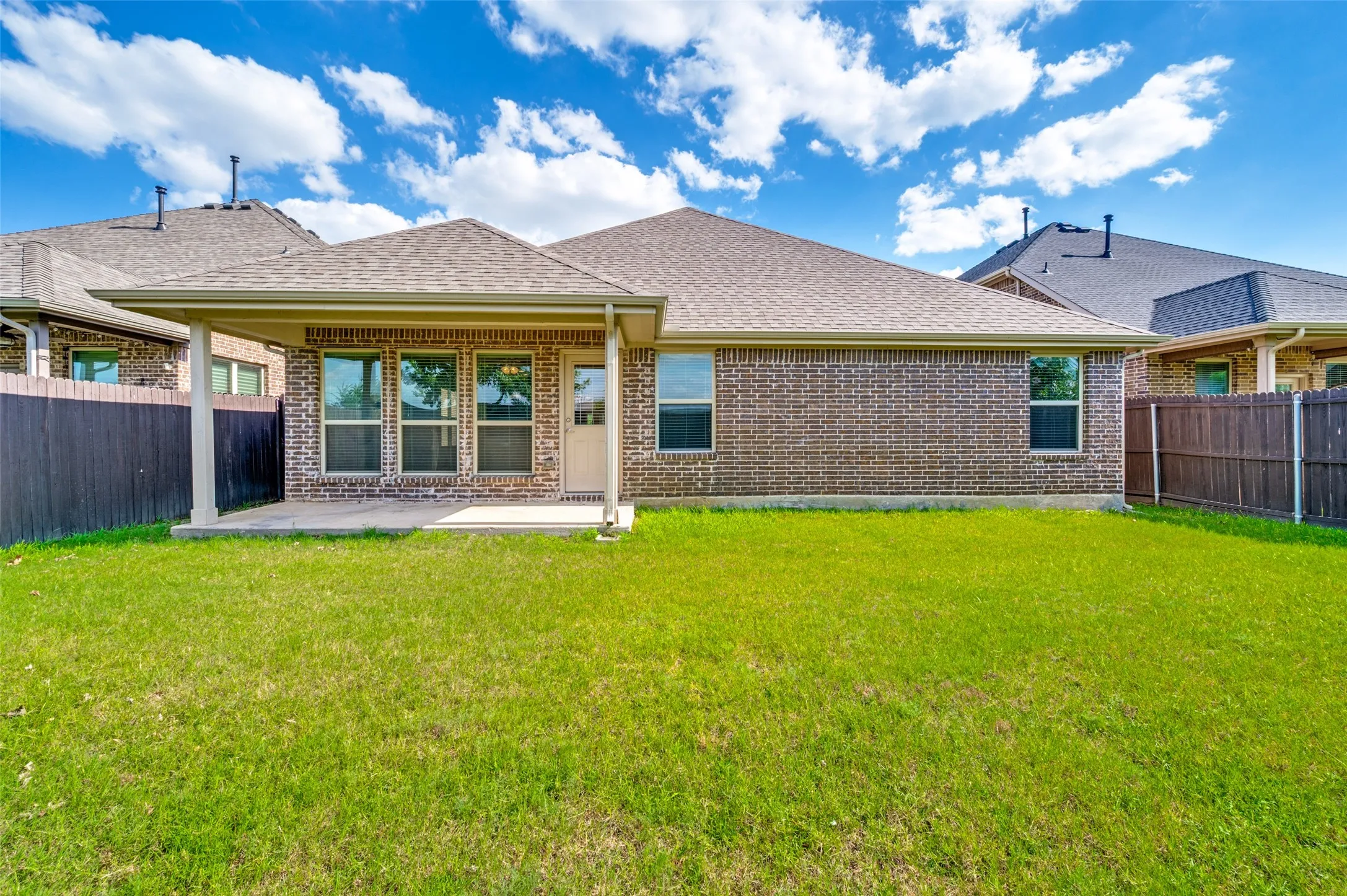Expansive backyard featuring a covered patio, brick exterior, multiple windows, and a privacy fence