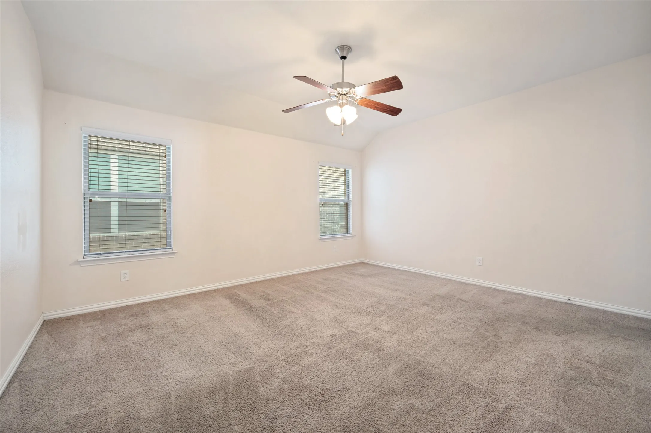 Spacious Master room featuring neutral carpet flooring, light-toned walls, two windows with blinds, a ceiling fan with light fixture, and a vaulted ceiling