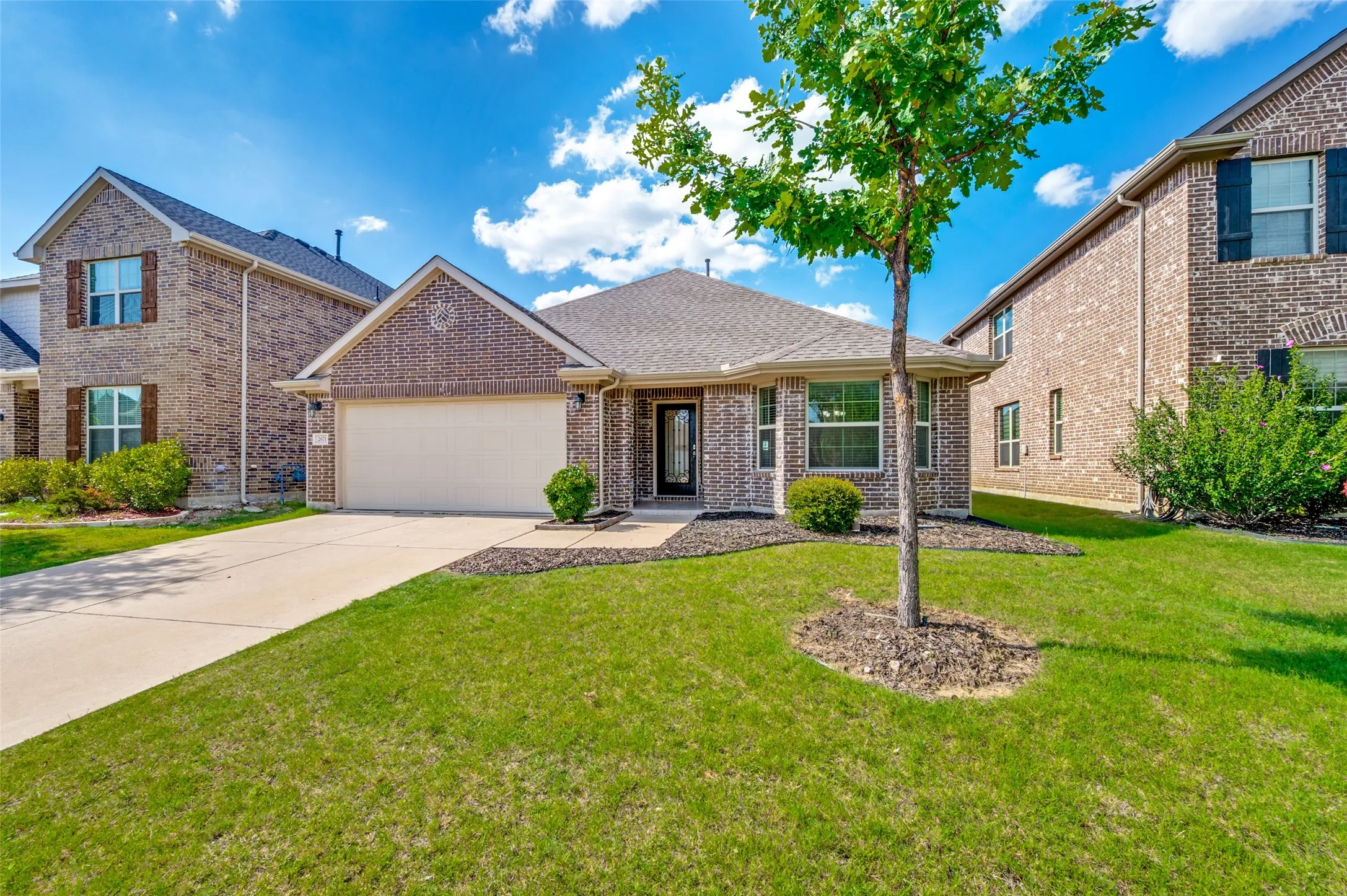 Brick facade single-story residence featuring a two-car garage, a paved driveway, and established landscaping