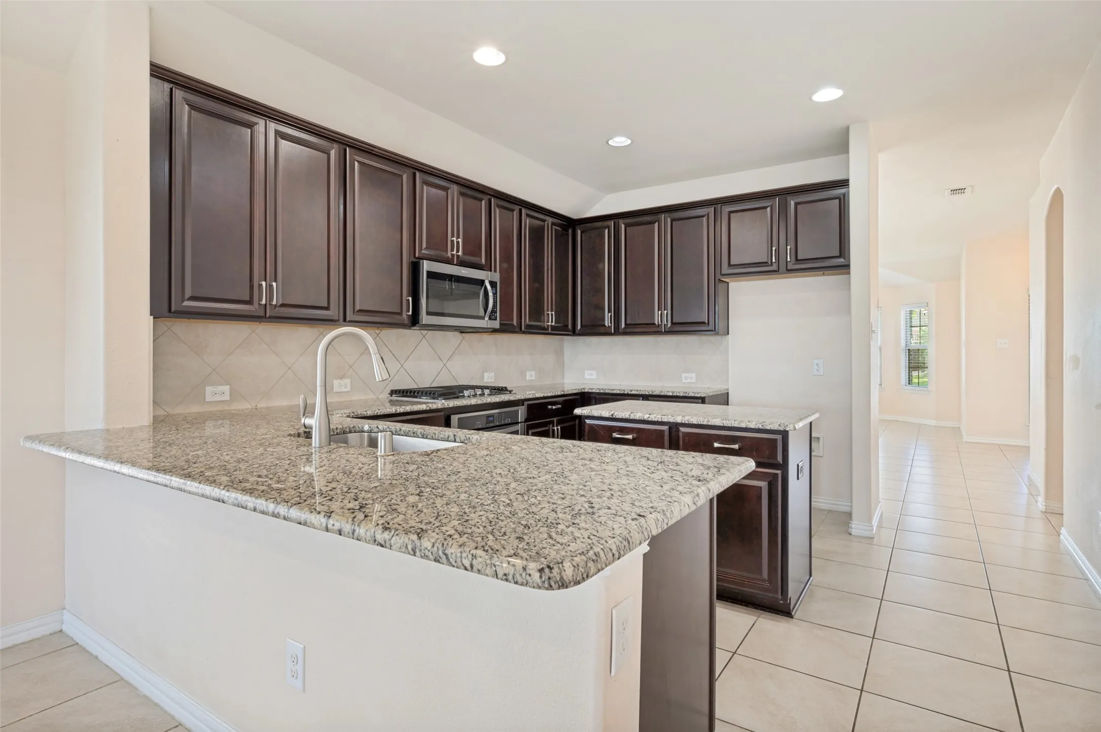 Kitchen featuring dark wood cabinetry, light-toned granite countertops, and a stainless steel sink with a gooseneck faucet