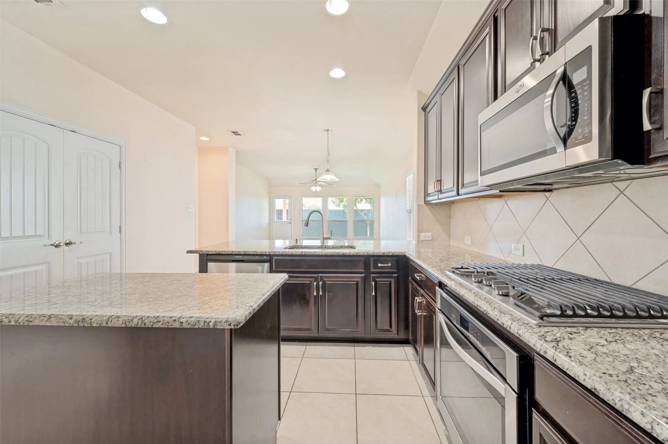 Kitchen featuring granite countertops, dark wood-finish cabinetry, stainless steel appliances, and tile flooring