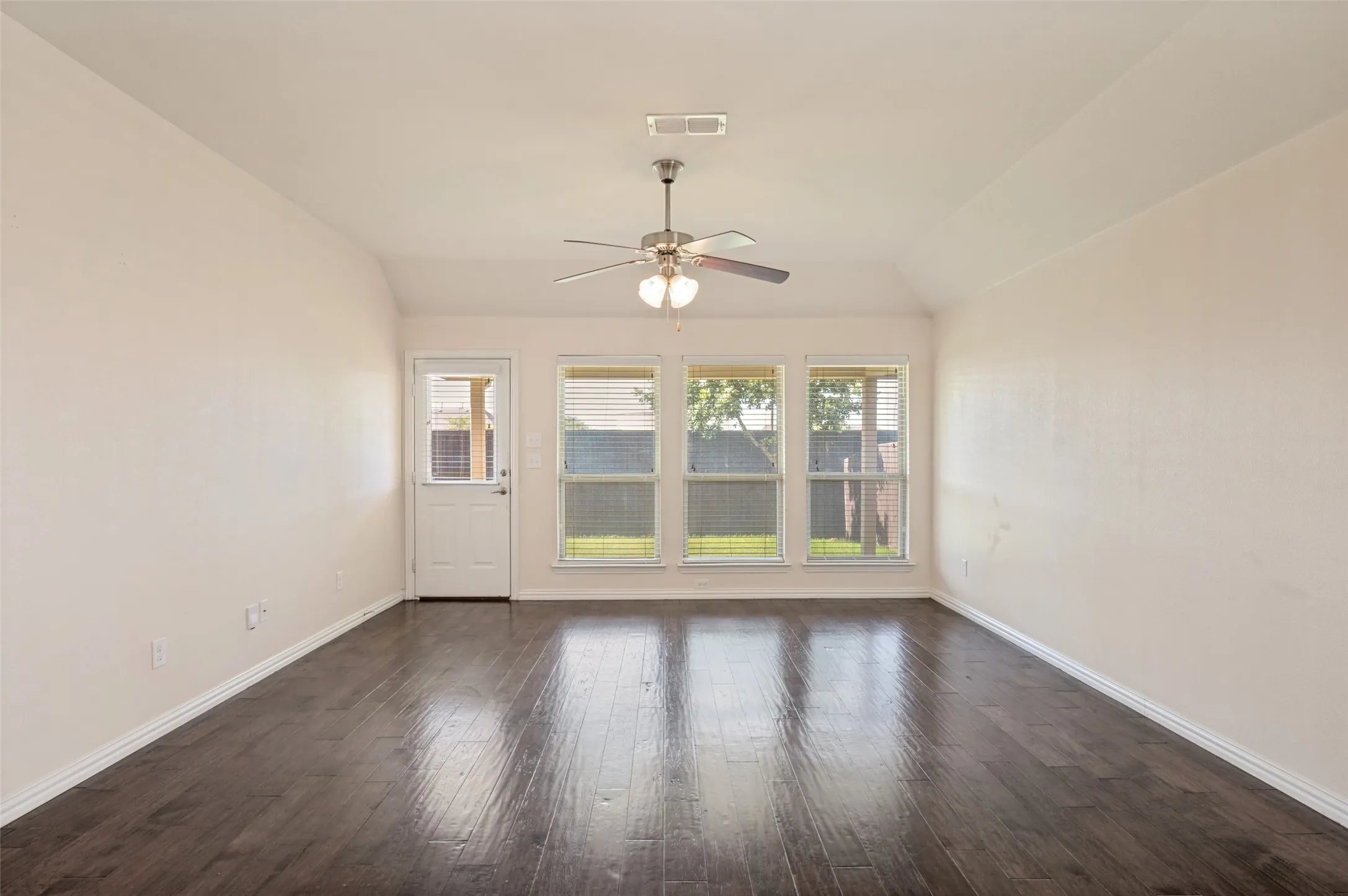 Open room featuring rich wood-finish flooring, a ceiling fan with integrated lighting, and a vaulted ceiling