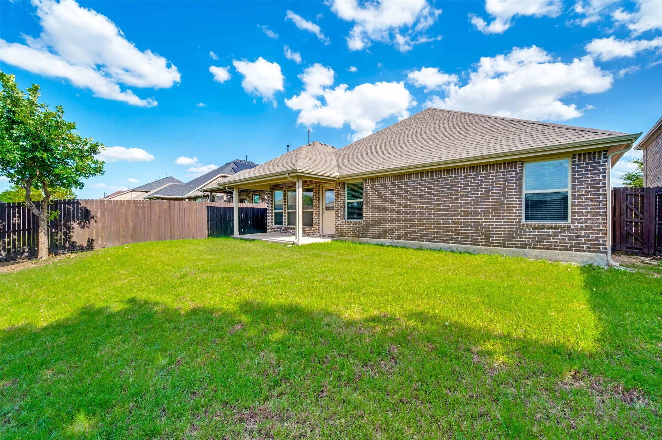 Expansive grassy yard featuring a covered patio, full brick exterior, composite shingle roof, and a wood privacy fence