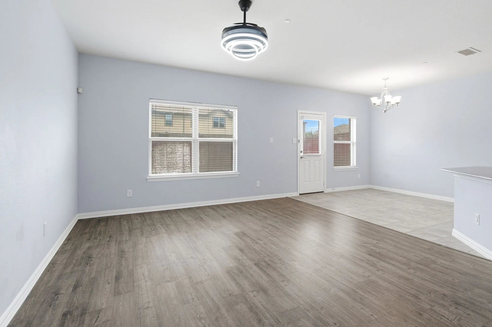 Living and dining areas with a beautiful lighting fixture and window views of the fenced backyard.