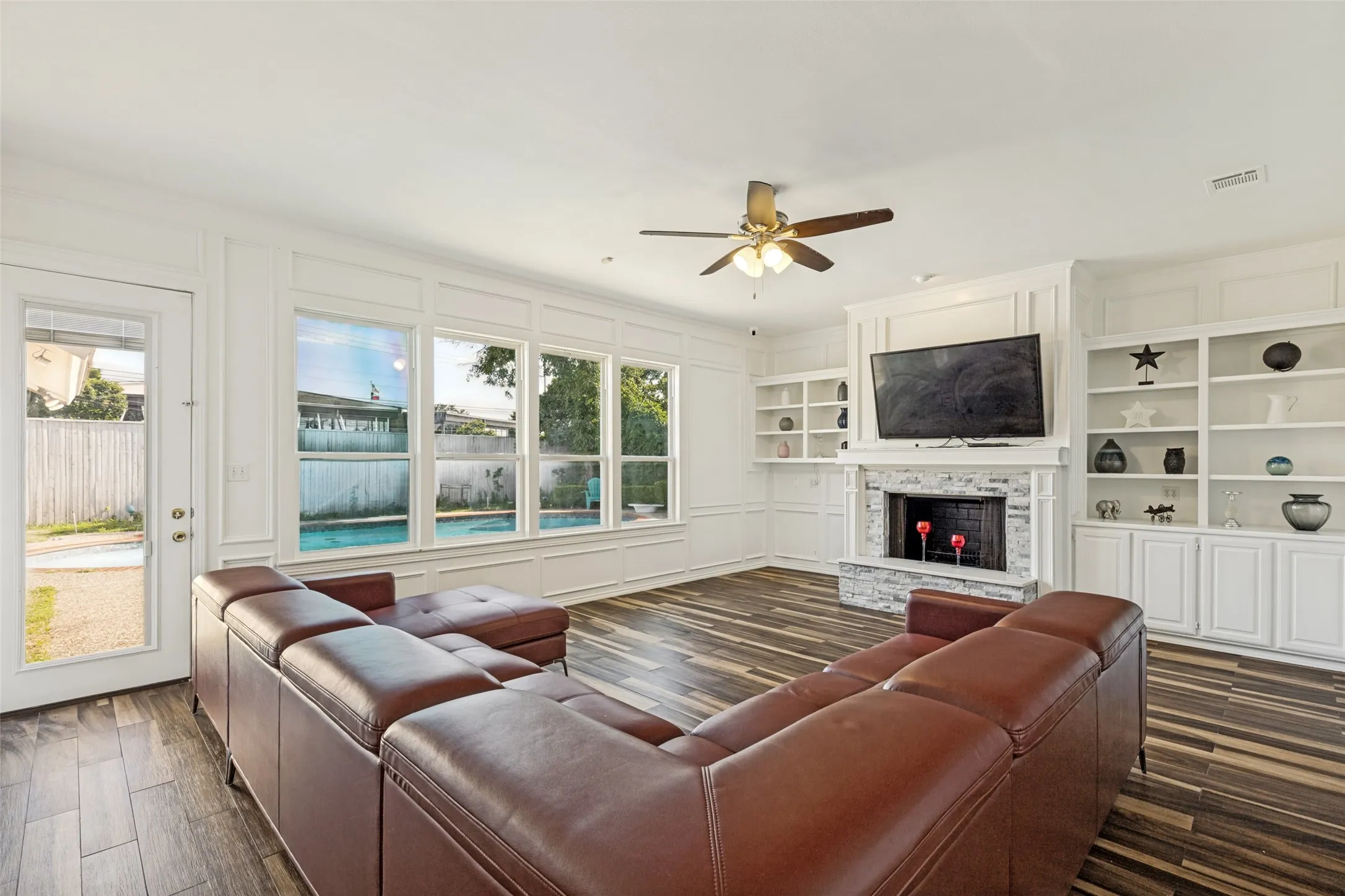 Spacious living area featuring wood-finish flooring, a white-painted brick fireplace with a mantel, and extensive built-in shelving