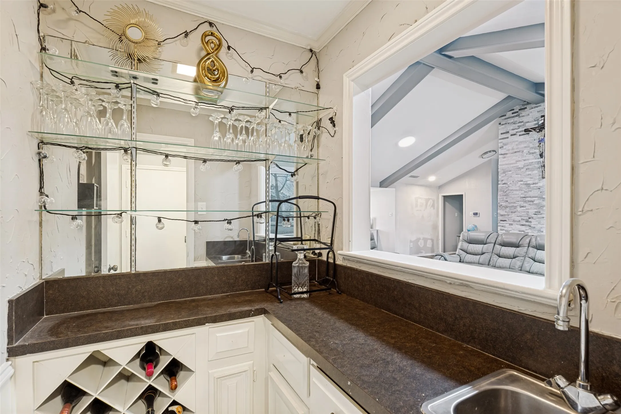 Wet bar featuring a stainless steel sink, chrome faucet, stone-finish countertops, mirrored backsplash, glass shelving, and integrated wine storage