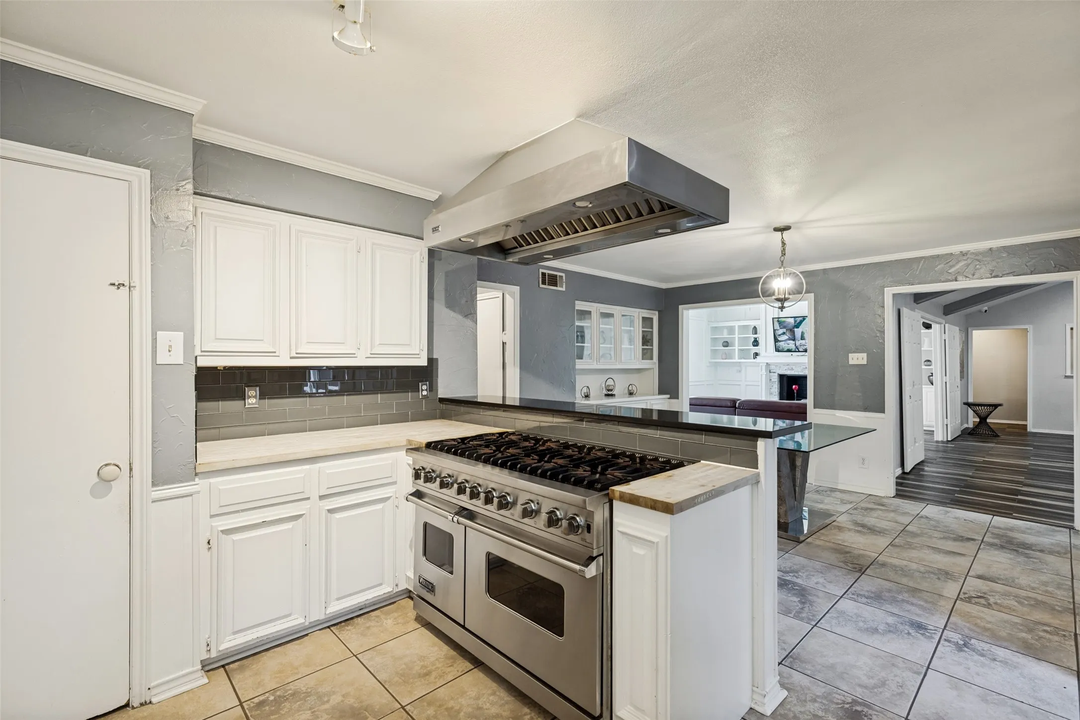 Gourmet kitchen featuring a professional-grade stainless steel range with a custom range hood, white cabinetry, dark subway tile backsplash, and light-toned countertops