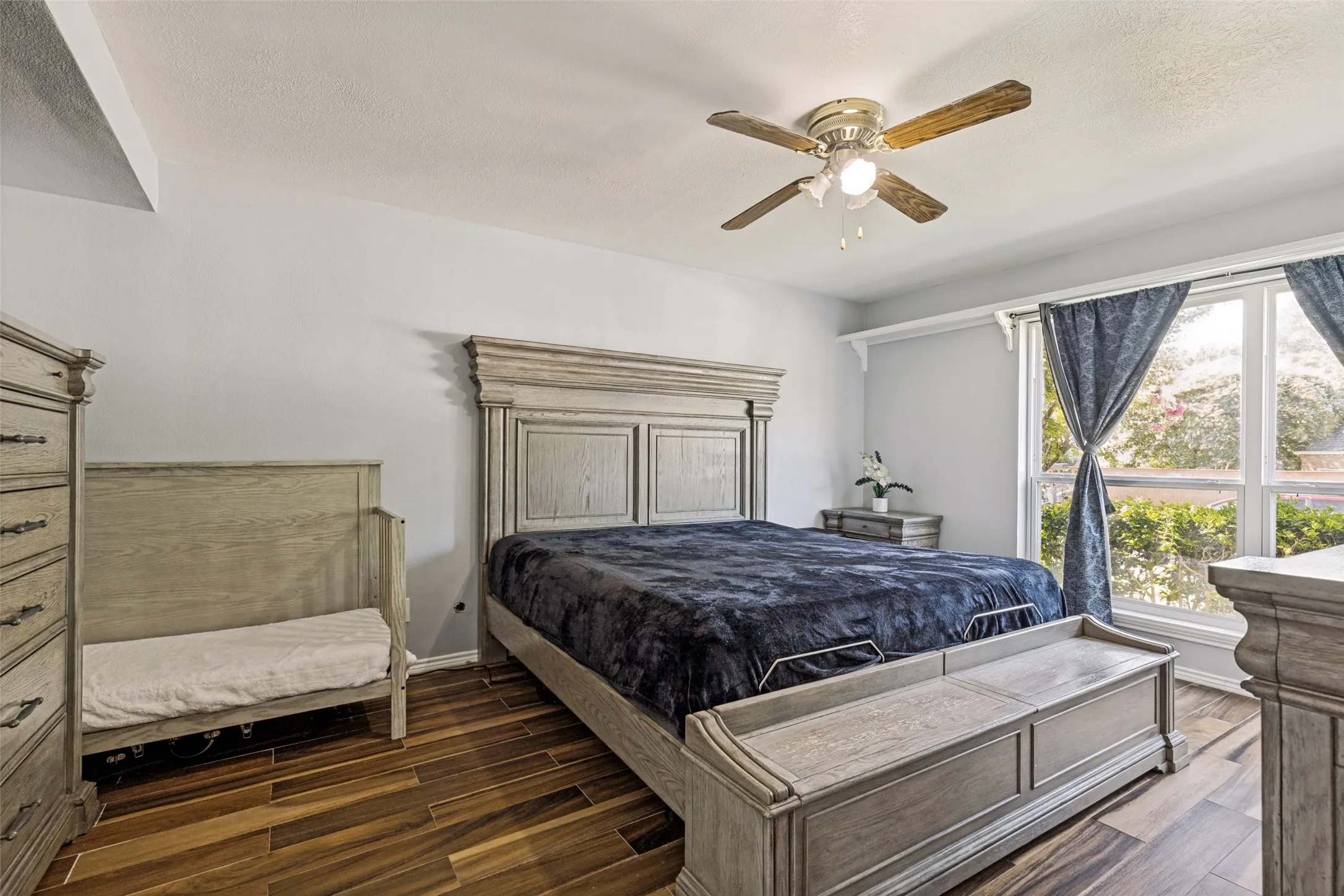 Spacious room featuring wood-finish flooring, a large window, and a ceiling fan with integrated lighting