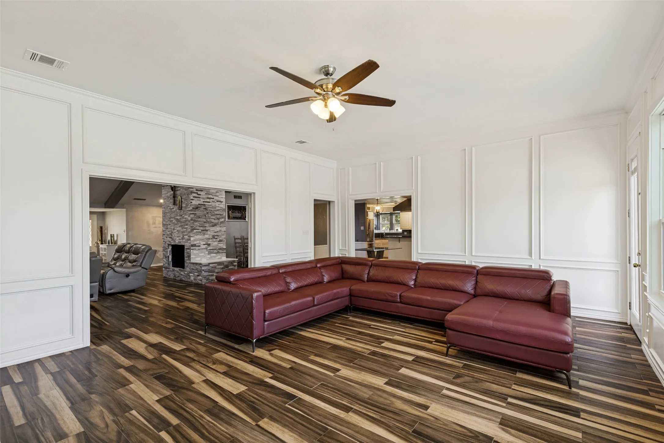 Living space featuring wood-finish flooring, white paneled walls, and a ceiling fan