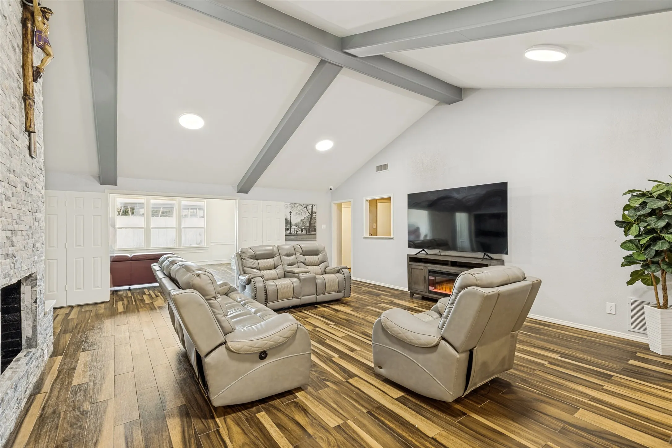 Vaulted ceilings with exposed beams, wood-finish flooring, a stone-clad fireplace, and recessed lighting
