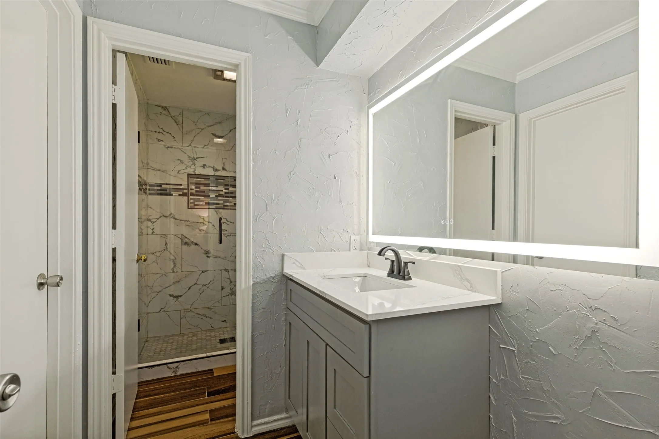 Contemporary bathroom vanity with a white countertop and integrated sink, illuminated by an LED-backlit mirror