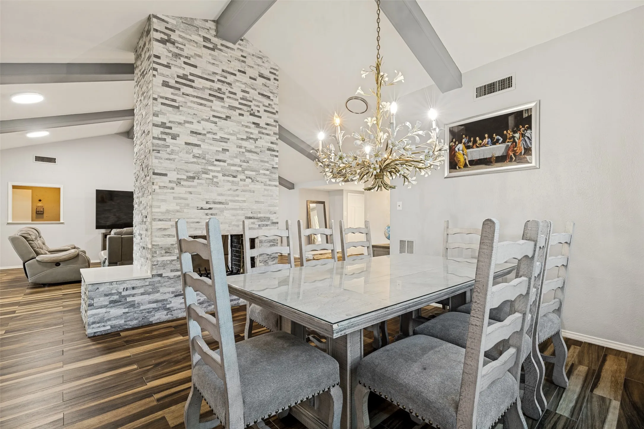 Dining area featuring a vaulted ceiling with exposed beams, a multi-tone stacked stone fireplace, wood-finish flooring, and recessed lighting
