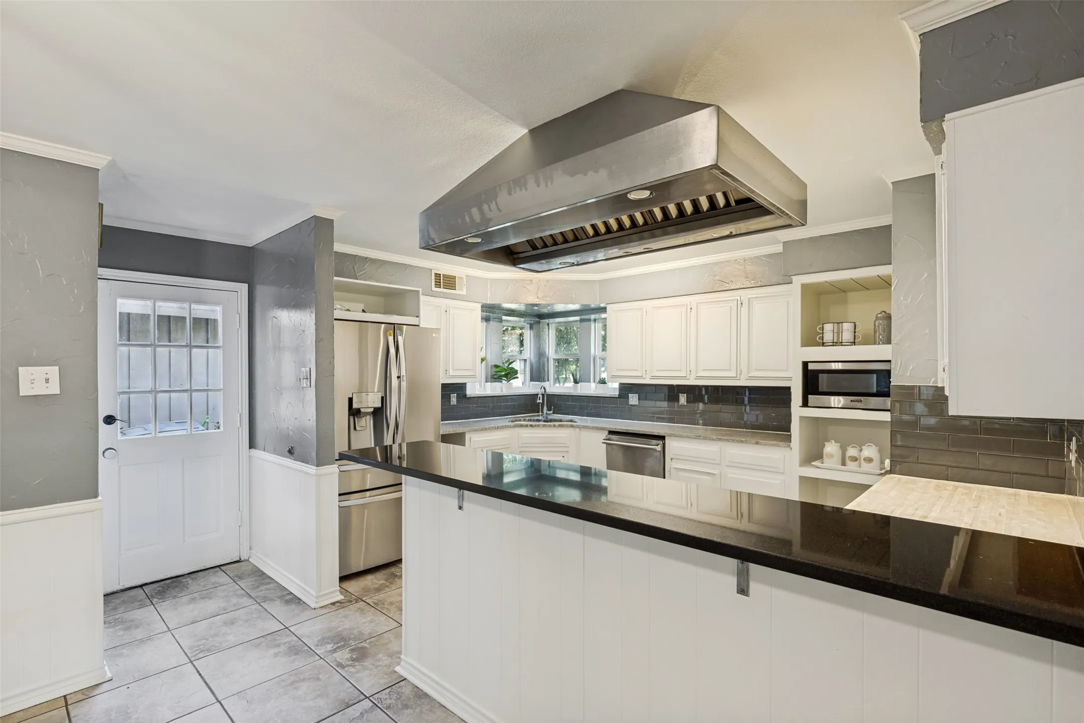 Kitchen featuring a large stainless steel range hood, white cabinetry, dark countertops, and tile flooring