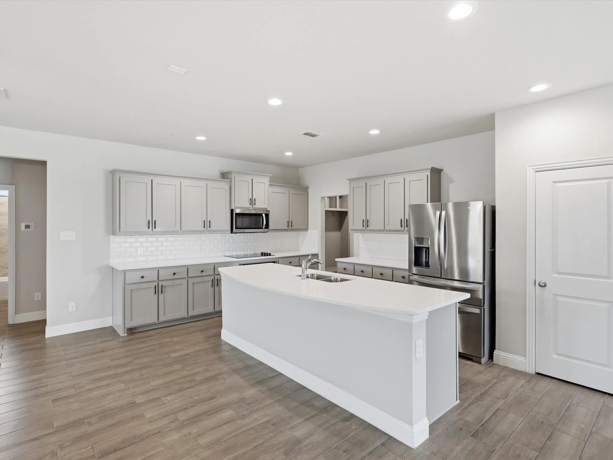 Kitchen featuring an island with white countertop, gray cabinetry, subway tile backsplash, stainless steel appliances, and wood-finish flooring