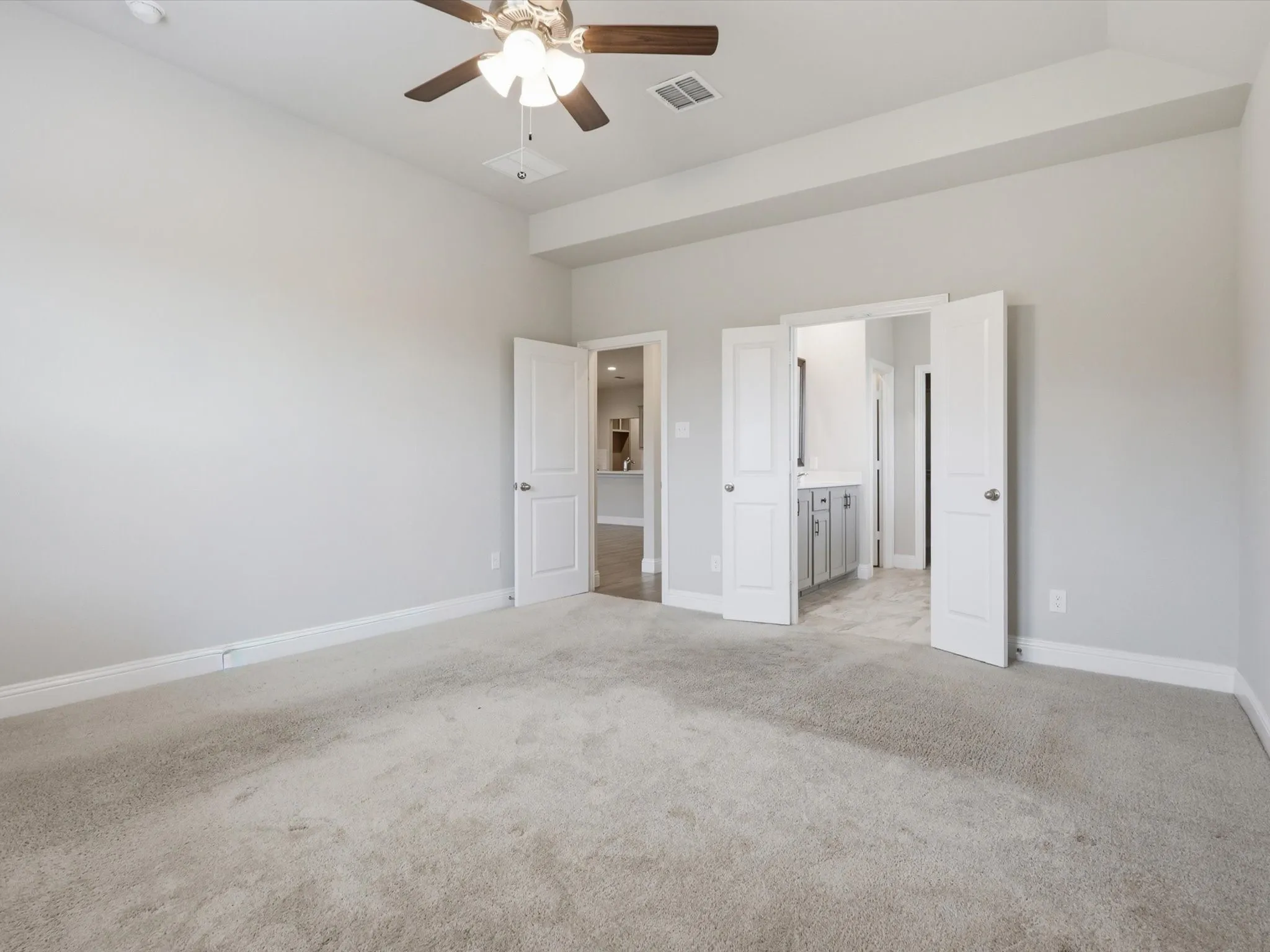 Carpeted room featuring a ceiling fan with light fixture, tray ceiling detail, and light gray wall paint