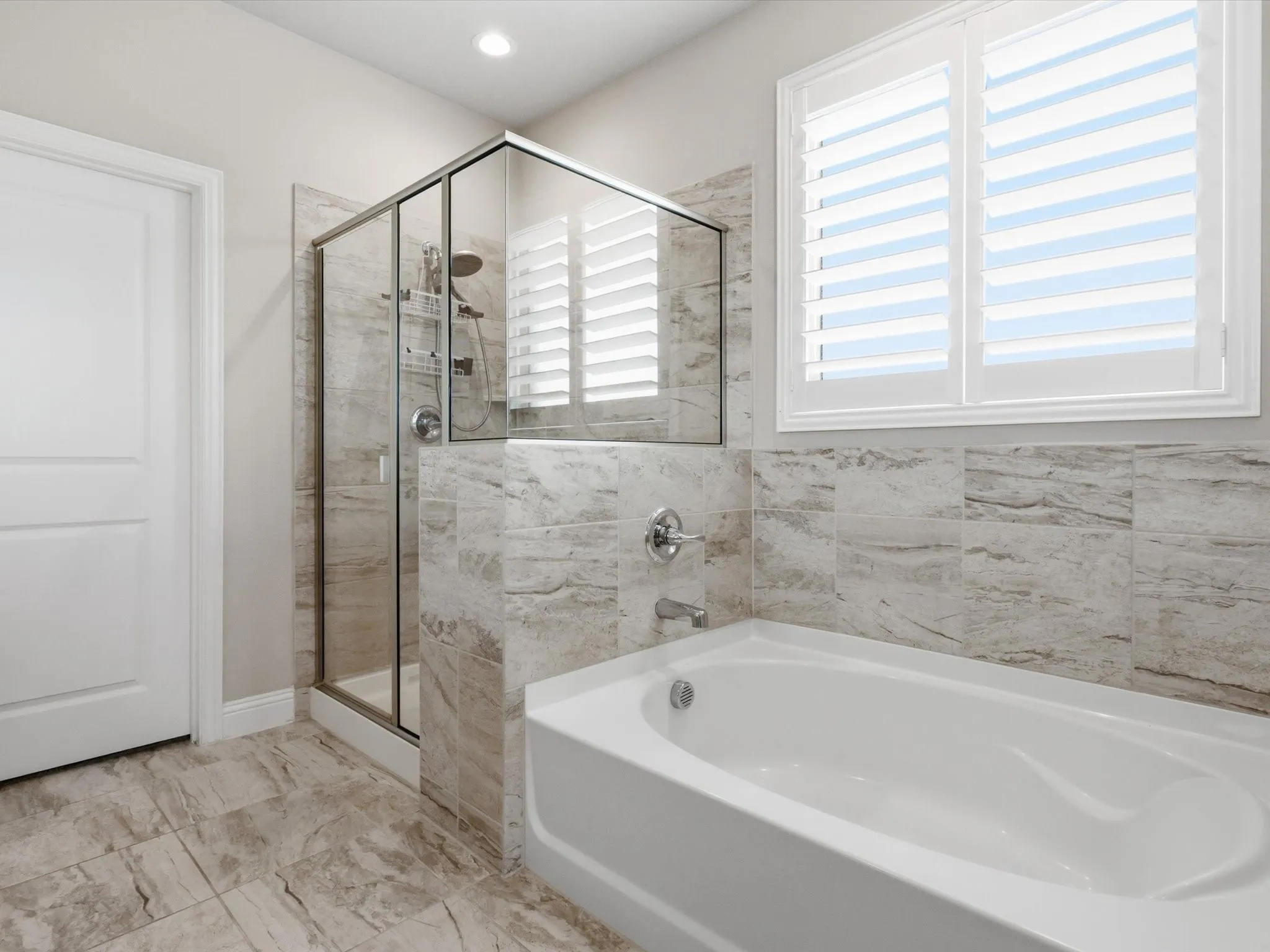 Bathroom featuring a built-in tub, separate glass-enclosed shower, tiled walls, and tiled flooring