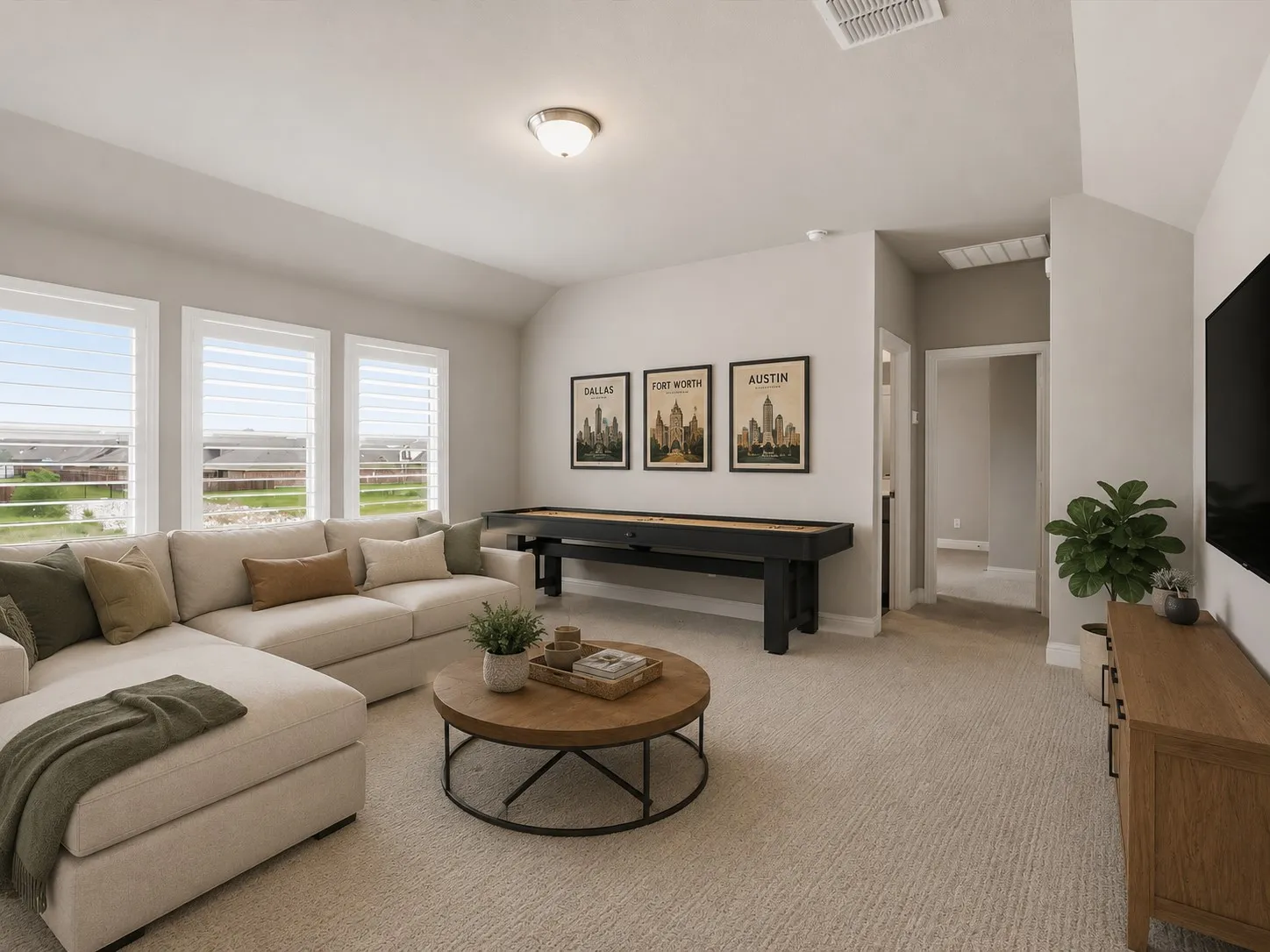 Spacious entertainment room featuring light gray walls, plush carpet flooring, a vaulted ceiling, and three large windows with white louvered shutters
