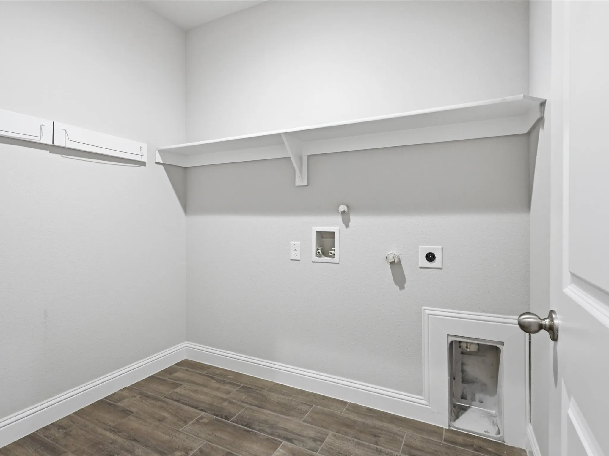 Utility room featuring wood-finish flooring, white baseboards, and a single wall shelf